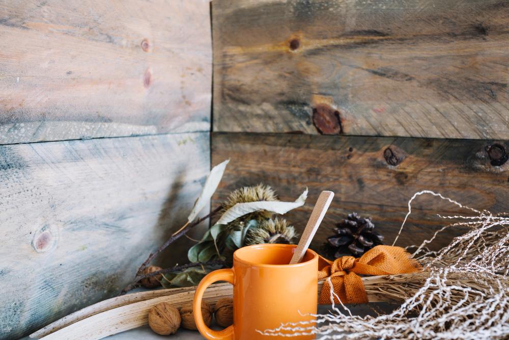 Tasse orange avec cuillère en bois posée sur une table rustique, entourée de noix, pommes de pin et éléments décoratifs naturels d’automne.