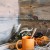 Tasse orange avec cuillère en bois posée sur une table rustique, entourée de noix, pommes de pin et éléments décoratifs naturels d’automne.